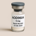 Glass vial labeled 'AOD9604 5 mg, Batch No.002, 23-06-2025' containing white lyophilized powder, sealed with a gray rubber stopper and matte silver cap, placed against a soft beige background