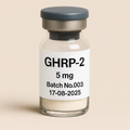 a clear glass vial containing off-white powder, labeled ‘GHRP-2 5 mg – Batch No.003 – 17-08-2025,’ sealed with a gray rubber stopper and matte aluminum cap, set against a soft beige background.”