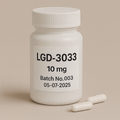 White plastic pill bottle labeled "LGD-3033, 10 mg, Batch No.003, 05-07-2025" on a beige background, with two white capsules lying beside it