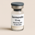 a clear glass vial containing off-white powder, labeled ‘Sermorelin 10 mg – Batch No.003 – 13-08-2025,’ sealed with a gray rubber stopper and matte cap, set against a soft beige background.”